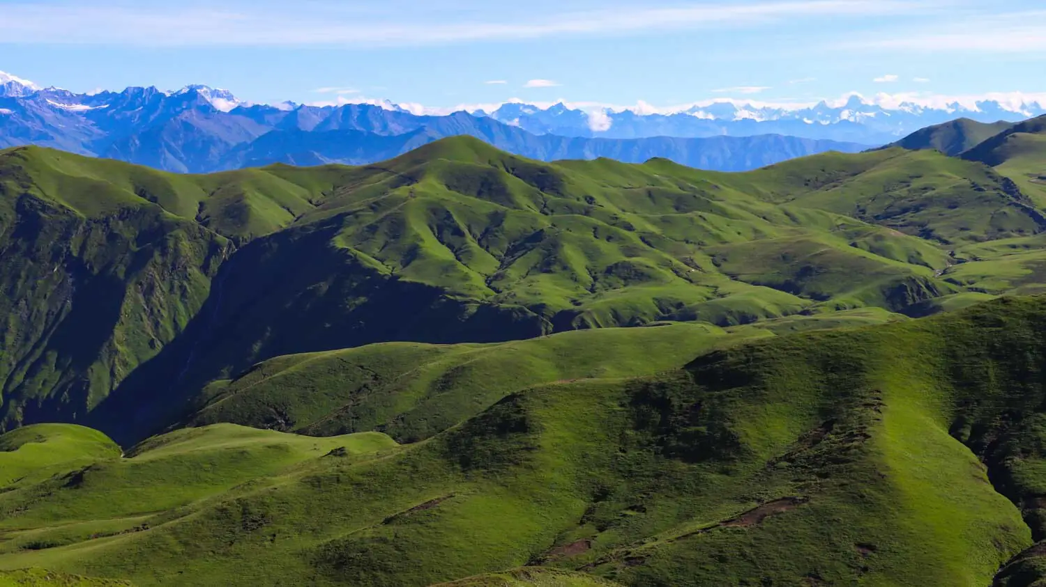 Rolling green highland meadows of Bajura with snow-capped Himalayan ranges on the horizon
