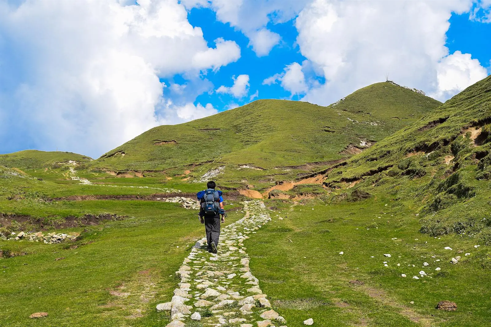 Stone-paved trail crossing green meadows toward rounded summits