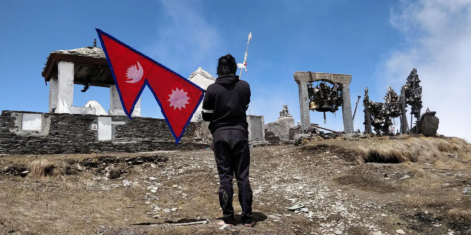 A pilgrim holding Nepal's flag before Badimalika Temple and its bells